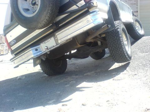 1985 Ford Bronco - Rear view of a 1985 Ford Bronco parked on an upward slope with a spare tire visible.