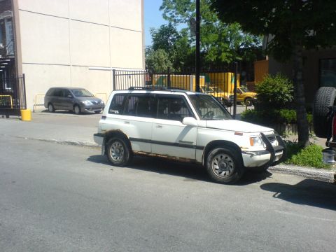 1985 Ford Bronco - This white SUV is parked on the street, showing signs of rust along its lower body panels.