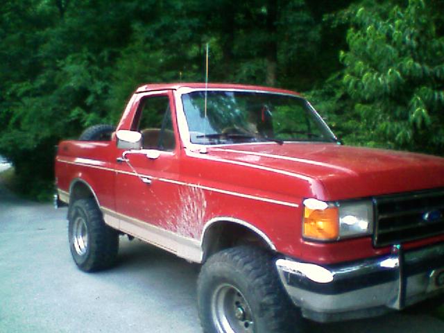 Red lifted Ford Bronco front three-quarter on pavement near trees