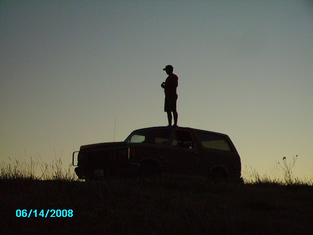Man on roof of a 1990s Ford Bronco at sunset