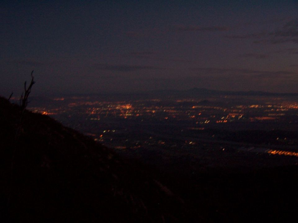 Distant city lights at dusk viewed from a dark hillside