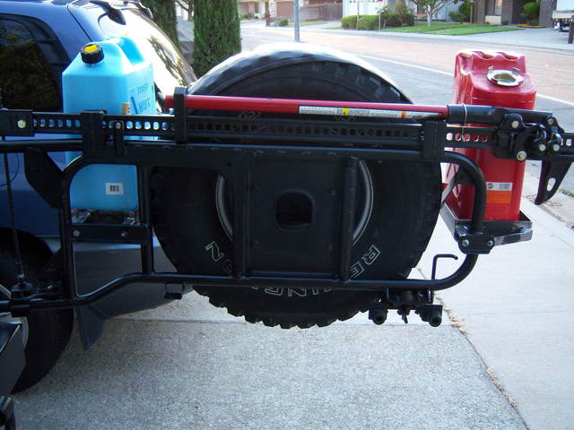 Rear of a blue SUV with spare tire, red jerry can, and blue water jug on a black carrier.