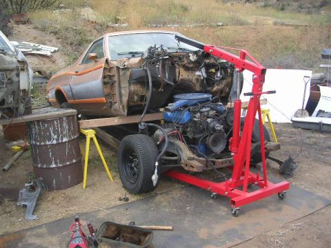 1975 Ford Ranchero - A disassembled 1970s Ford Ranchero is supported by jack stands and an engine hoist, with its engine and chassis exposed.