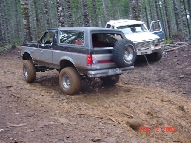Silver and black SUV with spare tire on rear, parked on dirt path with white SUV behind