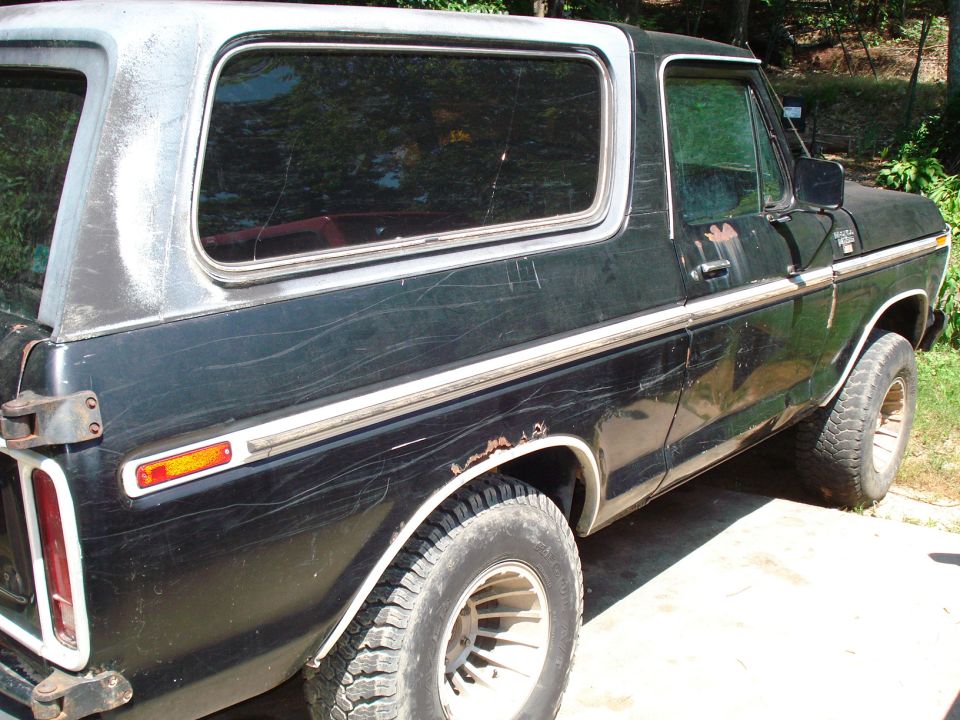 Black 1980s Ford Bronco, driver's side rear quarter panel, showing scratches and rust.