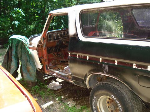 1989 Ford Bronco - The side profile of a dark green and white Ford Bronco is shown, with the driver's side door open and partially covered by a green tarp. Th…