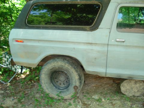 1989 Ford Bronco - The side view of a light-colored SUV shows its rear tire and part of the driver's side door. A red reflector is visible on the rear fender.