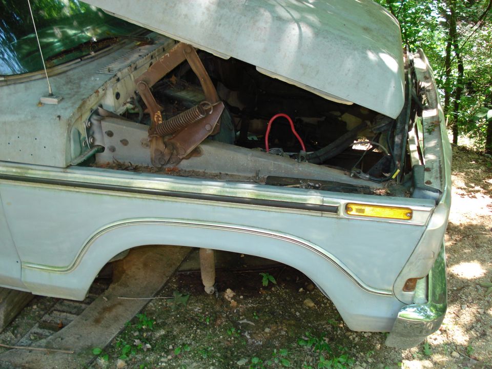 Light blue vehicle fender and open hood with rusty hinges, outdoors.