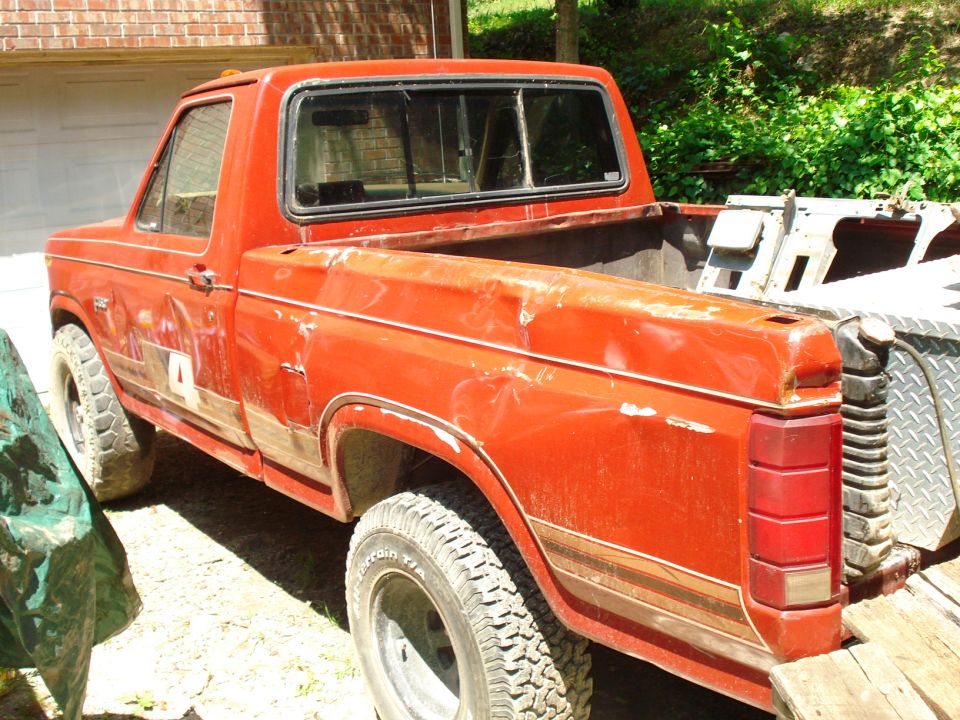 Faded red Ford pickup truck, rear passenger side, with toolbox and ramp.