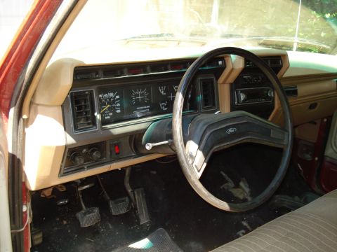 1989 Ford Bronco - The interior of a vintage Ford truck or SUV shows the dashboard with a steering wheel, instrument cluster, radio, and pedals. The tan and b…