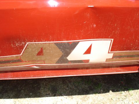 1989 Ford Bronco - A close-up view of the side of a red vehicle with a racing stripe graphic featuring the number 44. The vehicle shows signs of wear, includi…