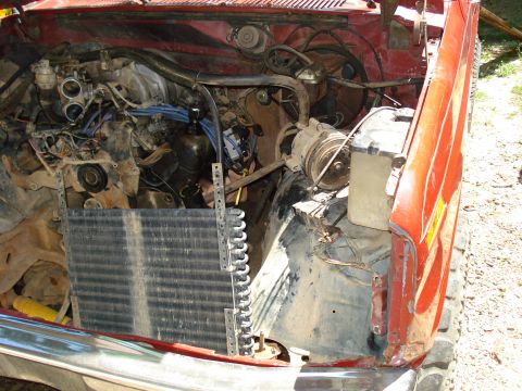 1989 Ford Bronco - The engine bay of a red 1989 Ford Bronco is shown with the hood removed, revealing the engine, radiator, and various hoses and wires. The v…