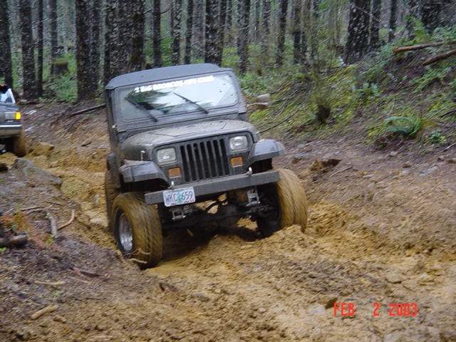Gray 1995 Jeep Wrangler driving through mud on a wooded trail