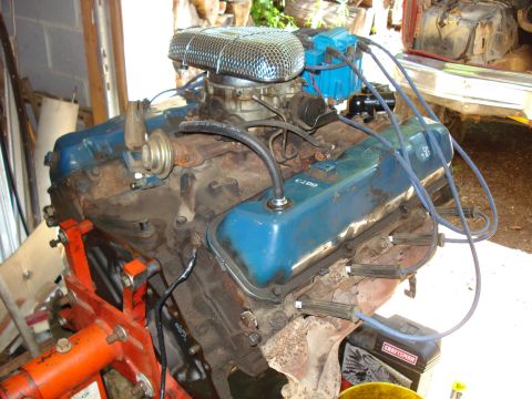 1989 Ford Bronco - A V8 engine with blue valve covers and an air cleaner is mounted on an orange engine stand. The engine has blue spark plug wires and a blue…