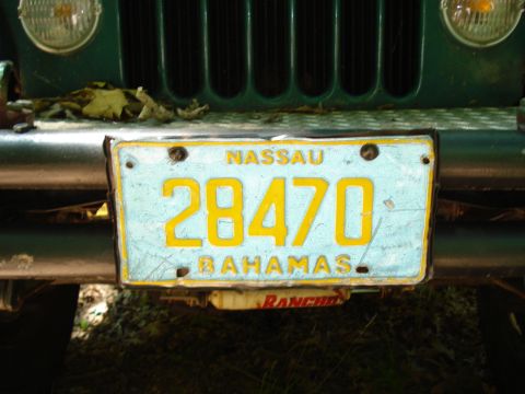 1989 Ford Bronco - A close-up of a light blue license plate with yellow text reading "NASSAU 28470 BAHAMAS" is mounted on the front bumper of a dark green veh…