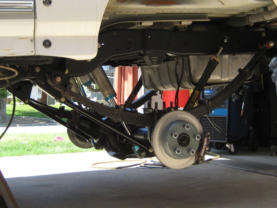 Underside of a white Ford Bronco showing suspension and rear brake assembly.