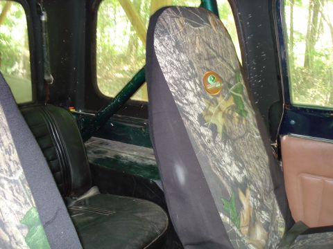 1989 Ford Bronco - The interior of a vehicle shows camouflage seat covers over black seats, with a roll cage visible. The view looks out through the windows a…