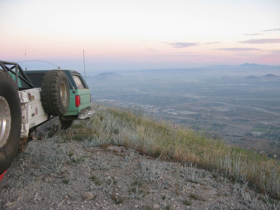 Rear view of a green Ford Bronco on a hillside at dusk.