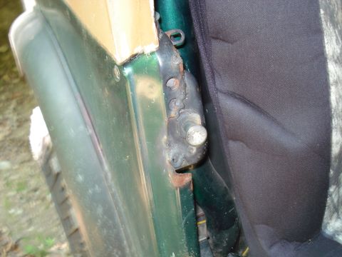 1989 Ford Bronco - A close-up view shows the rusted hinge area of a green vehicle door, with a black fabric seat visible to the right. The image focuses on th…