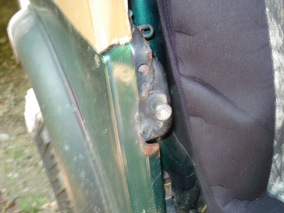 Close-up of rusted vehicle door hinge and black fabric seat.