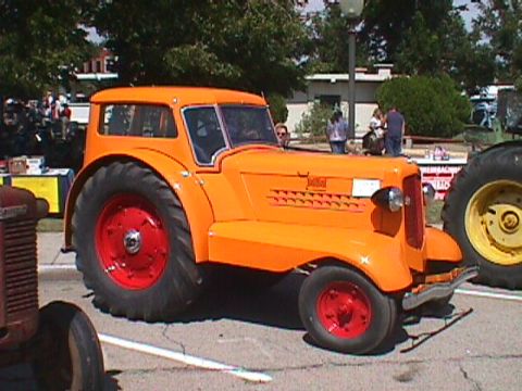 1991 Ford Bronco - A bright orange tractor with a closed cab is parked on pavement. The tractor has large rear wheels with red rims and smaller front wheels,…