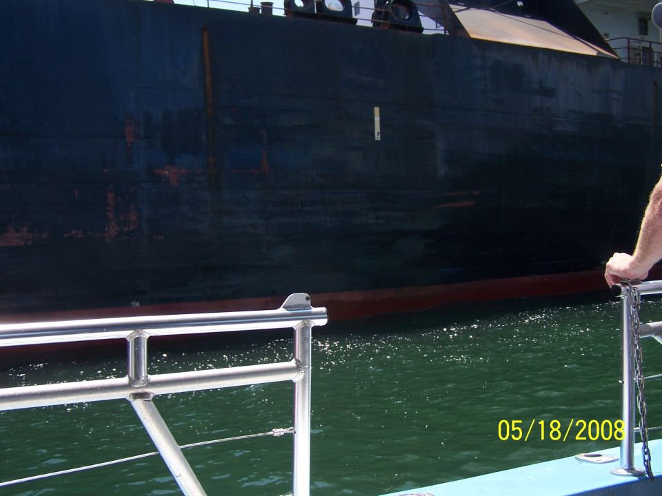 Photo of a large dark ship hull beside a boat's stainless railing