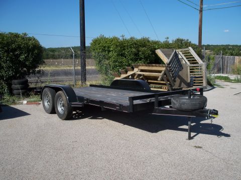 1996 Ford Bronco - A black utility trailer with a wooden deck is parked on an asphalt surface. The trailer has two axles with dual wheels and a spare tire mou…
