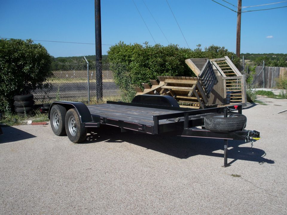 Black utility trailer with wooden deck, dual axles, and spare tire.