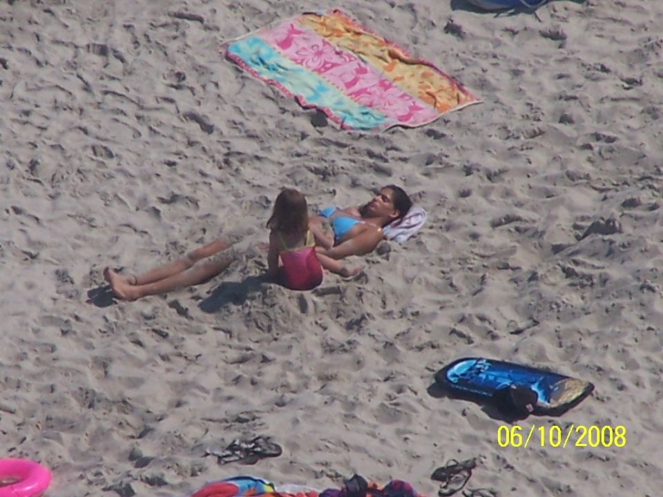 Adult and child sitting on the sand near a colorful beach towel
