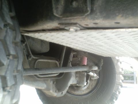 1991 Ford Bronco - A low-angle view of the undercarriage of a vehicle, showing the front wheel, suspension components, and a diamond plate skid plate.