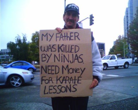 1991 Ford Bronco - A man holds a cardboard sign that reads "MY FATHER WAS KILLED BY NINJAS. NEED MONEY FOR KARATE LESSONS." He is wearing a baseball cap and a…
