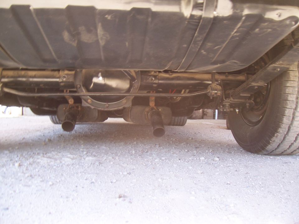 Underside of a vehicle showing rear differential, dual exhaust, leaf springs, and fuel tank.