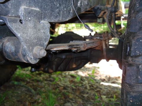 1989 Ford Bronco - The underside of a vehicle shows a leaf spring suspension system attached to a differential housing. A large, knobby tire is visible on the…