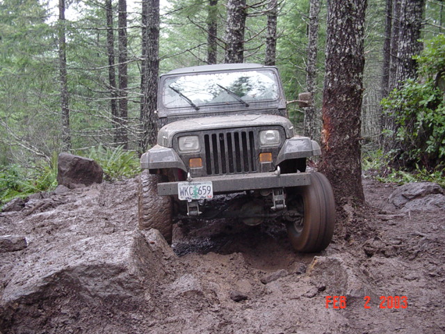Jeep Wrangler on a muddy, rocky trail in the woods
