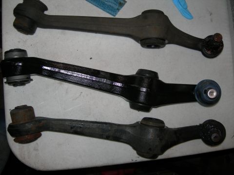 1992 Ford Taurus - Three control arms are laid out on a white surface. The top and bottom control arms appear to be older and rusted, while the middle control…