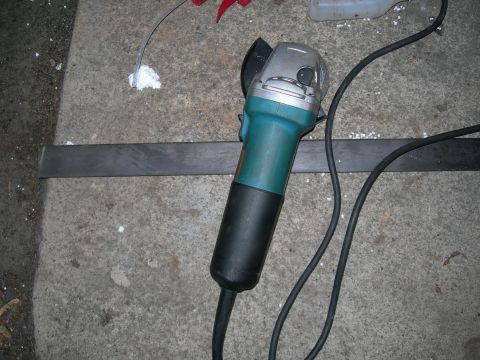 1992 Ford Taurus - An angle grinder with a teal and black body is resting on a concrete surface next to a metal bar. A black power cord snakes away from the t…