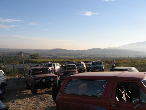 1996 Ford Bronco - A group of off-road vehicles are parked on a dirt lot overlooking a valley and mountains under a clear blue sky. The foreground features a…