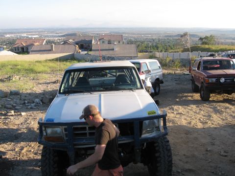 1996 Ford Bronco - A man wearing a baseball cap and a dark shirt stands next to a lifted white Ford Bronco with a blue brush guard. The vehicle is parked on a…