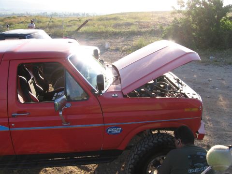 1996 Ford Bronco - A red Ford Bronco with its hood open is parked on a dirt road. A person is working on the front wheel of the vehicle.
