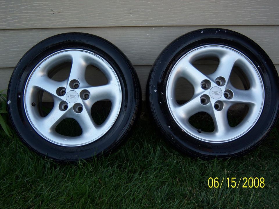 Two silver Ford alloy wheels with tires on grass.
