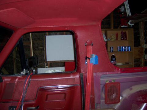 1991 Ford Bronco - The interior of a vehicle shows a red door panel, a red seatbelt, and a shelf with beverages in the background.
