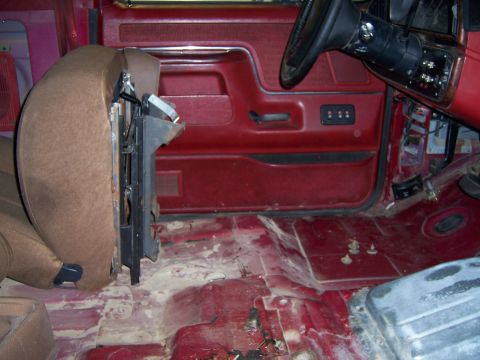 1991 Ford Bronco - The interior of a 1991 Ford Bronco shows a detached driver's seat and a red door panel with exposed floorboards.