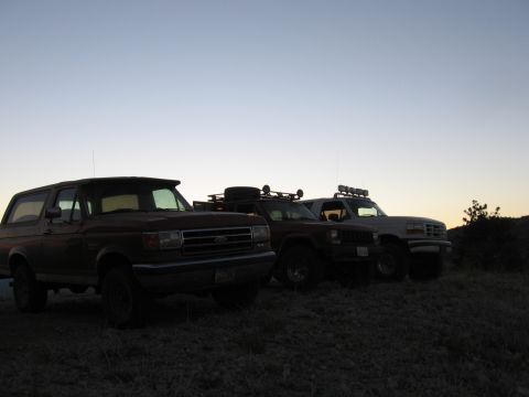 1996 Ford Bronco - Three SUVs, including a 1996 Ford Bronco, are parked on a hill as the sun sets.
