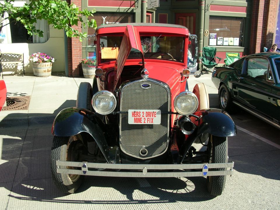 Red and black Ford Model A at a street show, hood side open, joke front plate