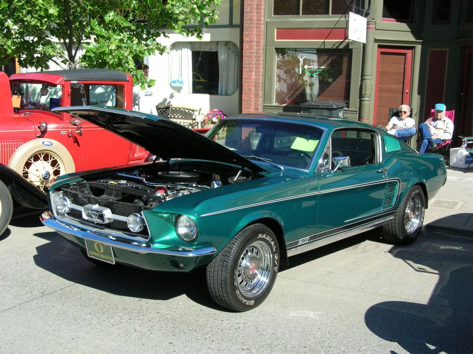 Green 1967 Ford Mustang fastback with hood open at a street car show, front three-quarter view