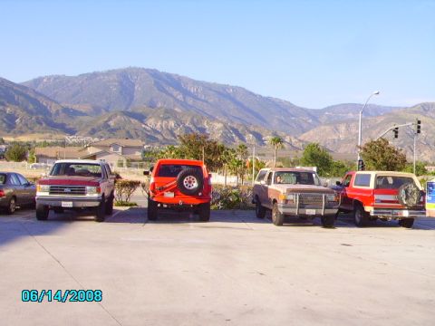 1990 Ford Bronco - Four Ford Bronco SUVs are parked in a lot under a clear blue sky.