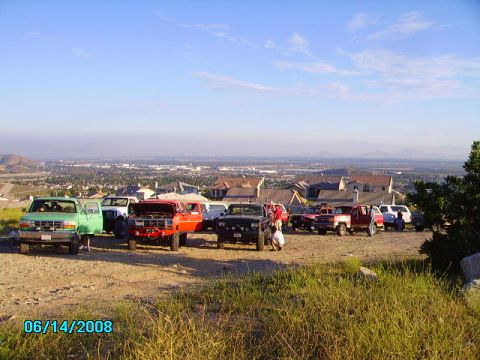 1990 Ford Bronco - A collection of vehicles are gathered on a hill with a town in the background.