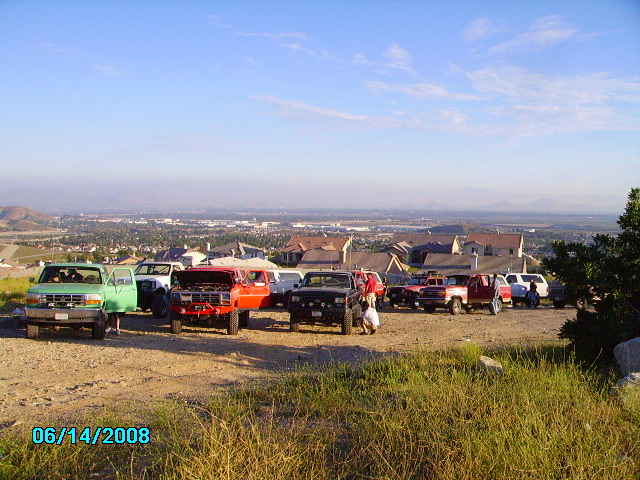 several trucks and SUVs parked on a dirt lot overlooking a town
