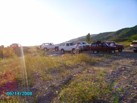 1990 Ford Bronco - A group of off-road vehicles are parked in a dusty lot on a sunny day.