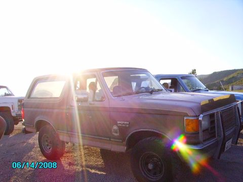 1990 Ford Bronco - A 1990 Ford Bronco is seen parked next to another vehicle under a bright sun.